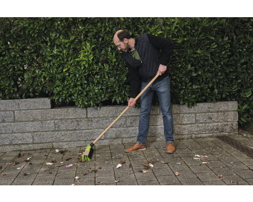 Osoba zametá listí pouličním koštětem.