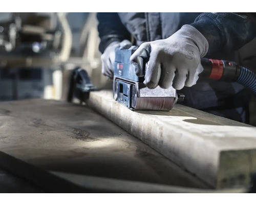 Řemeslník brousí dřevo pásovou bruskou