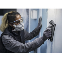 Osoba nosí ochranné pomůcky a hladí stěnu pomocí hladítka.