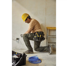 Elektrikář klečí a pracuje na elektrických vodičích s opaskem na nářadí a žlutou ochrannou helmou.