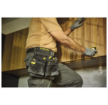 Řemeslník s pouzdrem na nářadí a svinovacím metrem při montáži dřevěných skříní