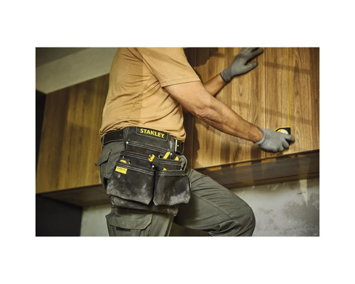 Řemeslník s pouzdrem na nářadí a svinovacím metrem při montáži dřevěných skříní