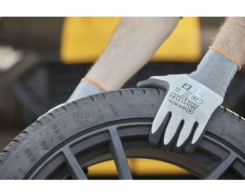 Osoba s ochrannými rukavicemi drží černou pneumatiku.