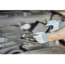 Mechanik s ochrannými rukavicemi používá tablet u motoru automobilu.