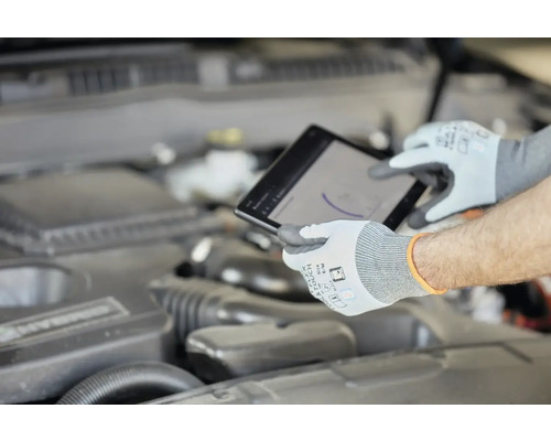 Mechanik s ochrannými rukavicemi používá tablet u motoru automobilu.