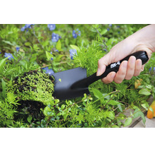 Osoba drží v zahradě ruční lopatku s rostlinou.