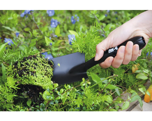 Osoba drží v zahradě ruční lopatku s rostlinou.