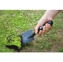 Osoba drží černou zahradní lopatku s kusem hlíny a rostlinami.