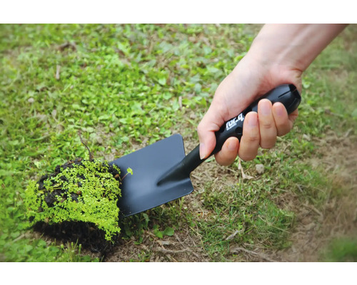 Osoba drží černou zahradní lopatku s kusem hlíny a rostlinami.