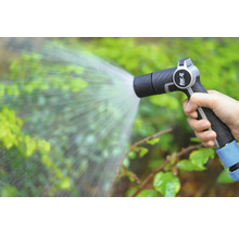 Ruka drží zahradní stříkací pistoli, která stříká vodu na rostliny