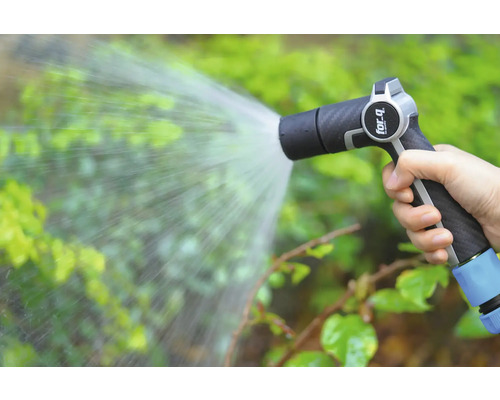 Ruka drží zahradní stříkací pistoli, která stříká vodu na rostliny