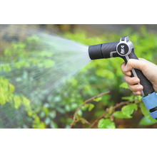 Ruka drží zahradní stříkací pistoli a zalévá rostliny.