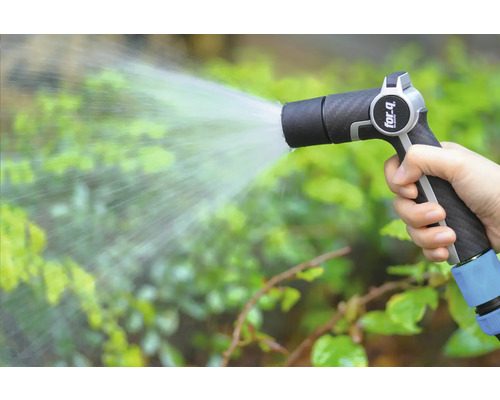Ruka drží zahradní stříkací pistoli a zalévá rostliny.