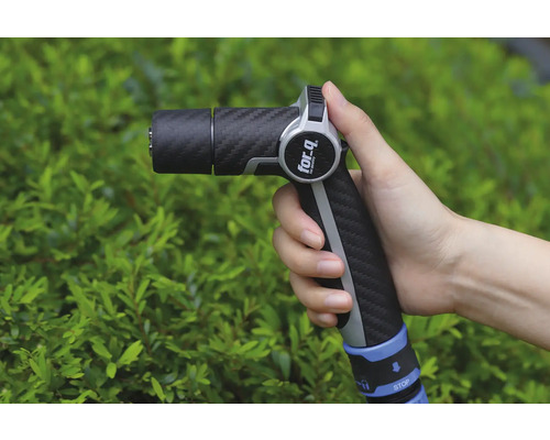 Ruka drží zahradní stříkací pistoli značky For Q před zeleným keřem