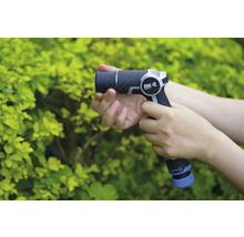 Osoba drží zahradní stříkací pistoli značky for_q před zeleným keřem.