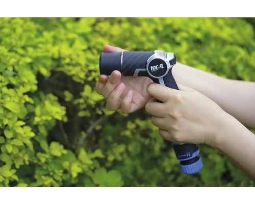 Osoba drží zahradní stříkací pistoli značky for_q před zeleným keřem.