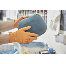 Muž v rukavicích drží vzduchový filtr nad kbelíkem.