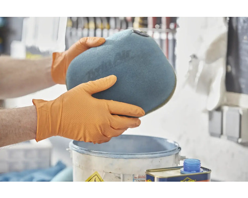 Muž v rukavicích drží vzduchový filtr nad kbelíkem.