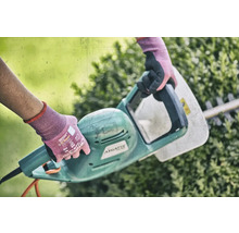 Osoba používá elektrické nůžky na živý plot k úpravě živého plotu.