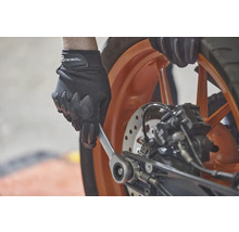 Osoba v rukavicích používá klíč na motocyklu.