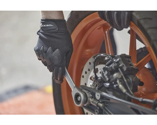 Osoba v rukavicích používá klíč na motocyklu.