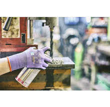 Osoba s ochrannými rukavicemi drží plechovku s rozprašovačem u vrtačky.