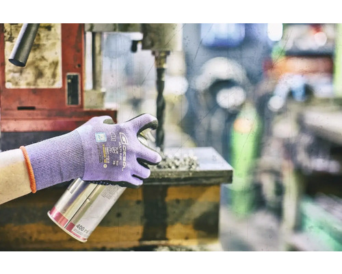 Osoba s ochrannými rukavicemi drží plechovku s rozprašovačem u vrtačky.