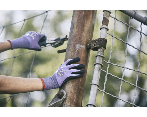 Osoba v rukavicích pracuje s kleštěmi na kovovém plotě.