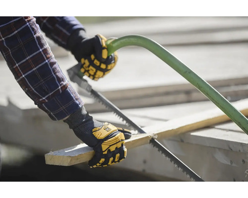Osoba řeže kus dřeva ruční pilou a má na sobě pracovní rukavice.