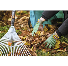 Osoba s hráběmi na listí a zahradními rukavicemi odstraňuje listí