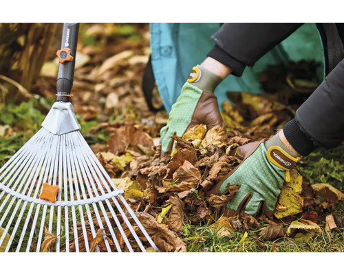 Osoba s hráběmi na listí a zahradními rukavicemi odstraňuje listí