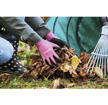 Osoba v zahradních rukavicích sbírá listí s hráběmi a vakem na listí v pozadí