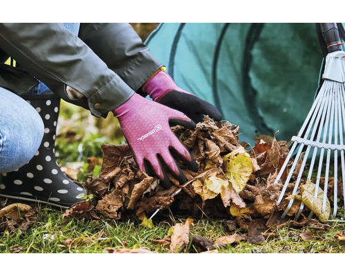 Osoba v zahradních rukavicích sbírá listí s hráběmi a vakem na listí v pozadí