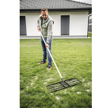 Muž používá travní válec pro údržbu trávníku na zahradě.