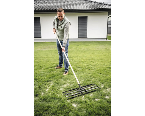 Muž používá travní válec pro údržbu trávníku na zahradě.