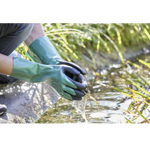 Osoba s vodotěsnými zahradními rukavicemi čistí zahradní jezírko