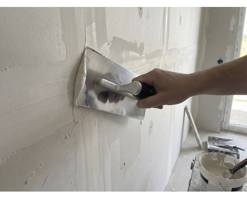 Řemeslník vyhlazuje stěnu pomocí hladítka a omítky