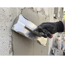 Řemeslník hladí omítku hladítkem na zdi.