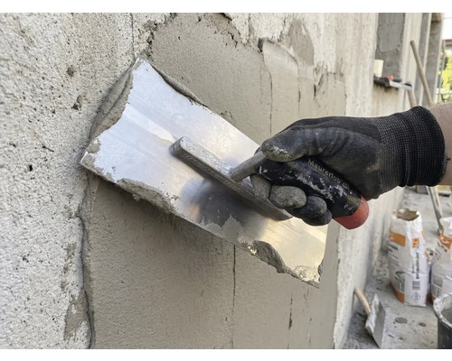 Řemeslník hladí omítku hladítkem na zdi.