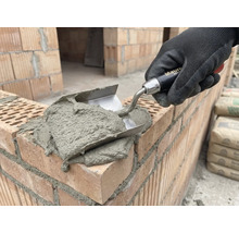 Zednická ruka s lžící nanáší maltu na cihly