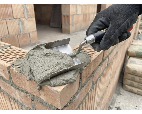 Zednická ruka s lžící nanáší maltu na cihly