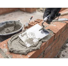 Zedník při práci s lžící, maltou a cihlami