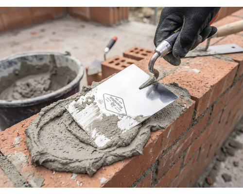 Zedník při práci s lžící, maltou a cihlami