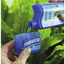 Přípravek na úpravu vody JBL Biotopol se nalévá do dávkovacího uzávěru, v pozadí akvarijní rostliny.