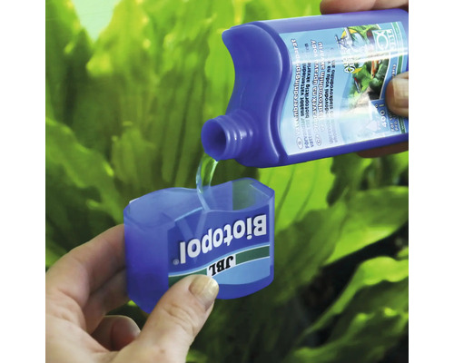 Přípravek na úpravu vody JBL Biotopol se nalévá do dávkovacího uzávěru, v pozadí akvarijní rostliny.