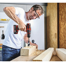 Muž vrtá otvor do kusu dřeva pomocí akumulátorového šroubováku