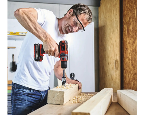 Muž vrtá otvor do kusu dřeva pomocí akumulátorového šroubováku