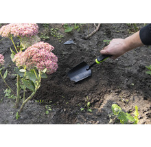 Zahradní scéna s rukou, která zapichuje sázecí lopatku do země