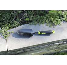 Zahradní lopatka na zdi s rostlinami v pozadí