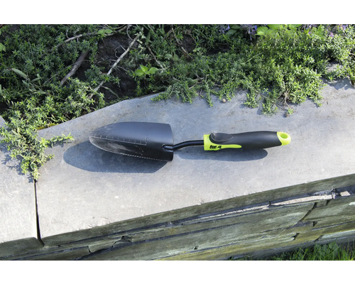 Zahradní lopatka na zdi s rostlinami v pozadí